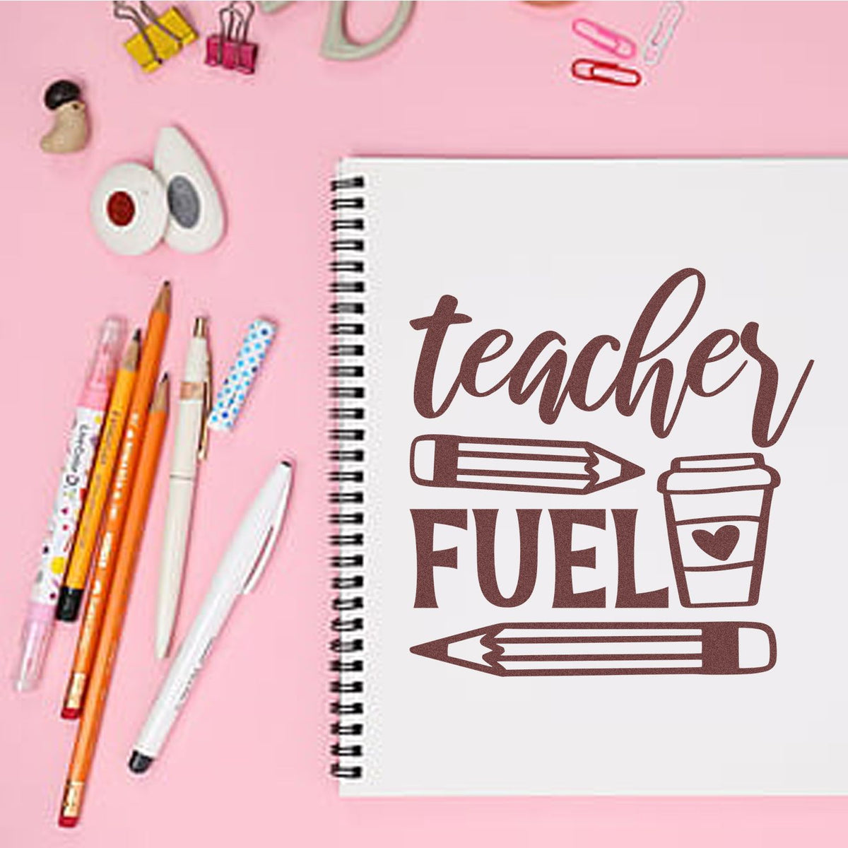 Pink teacher-themed stamp and seal design on spiral notebook, with brown teacher fuel lettering, pencils, and pens.