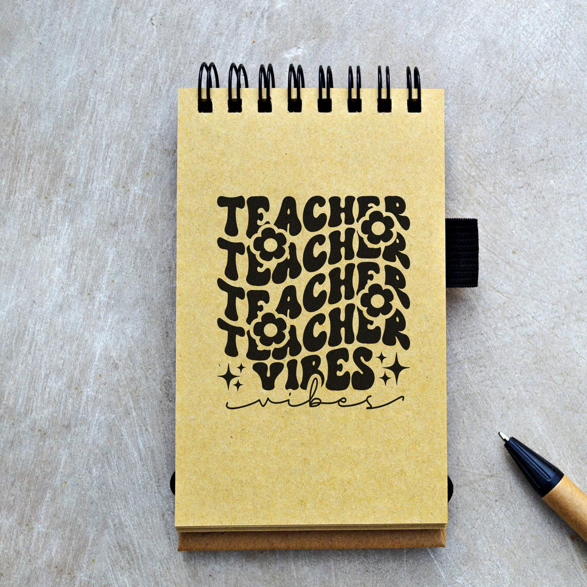Yellow spiral notebook with black Teacher Vibes stamp design, floral accents, and black pen, showcasing stamp and seal products.