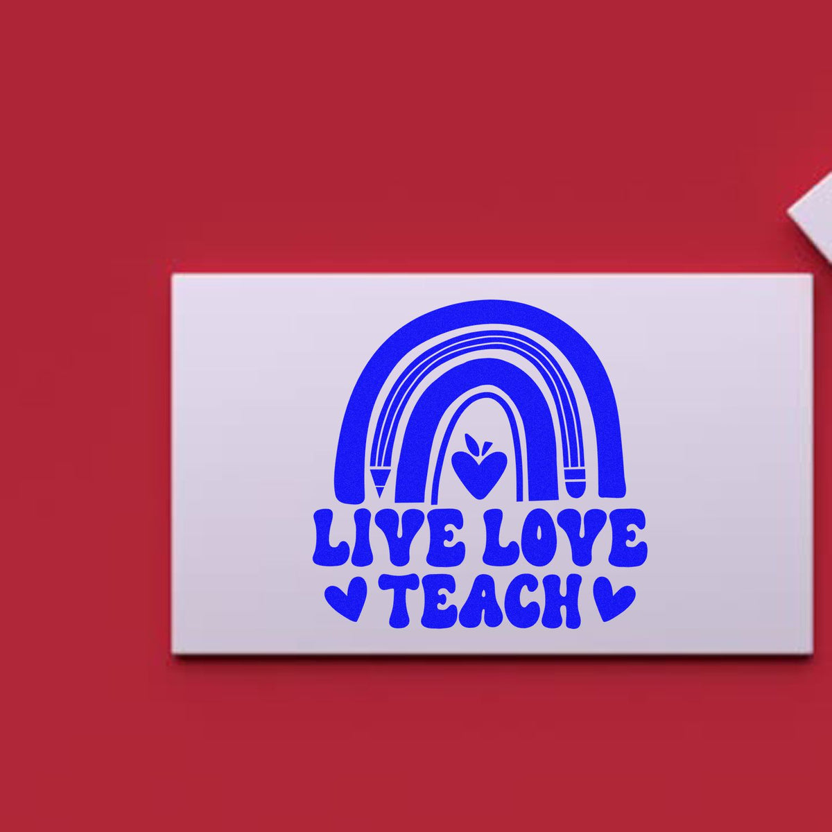 Blue LIVE LOVE TEACH stamp seal with rainbow heart on white card, set against a red background.