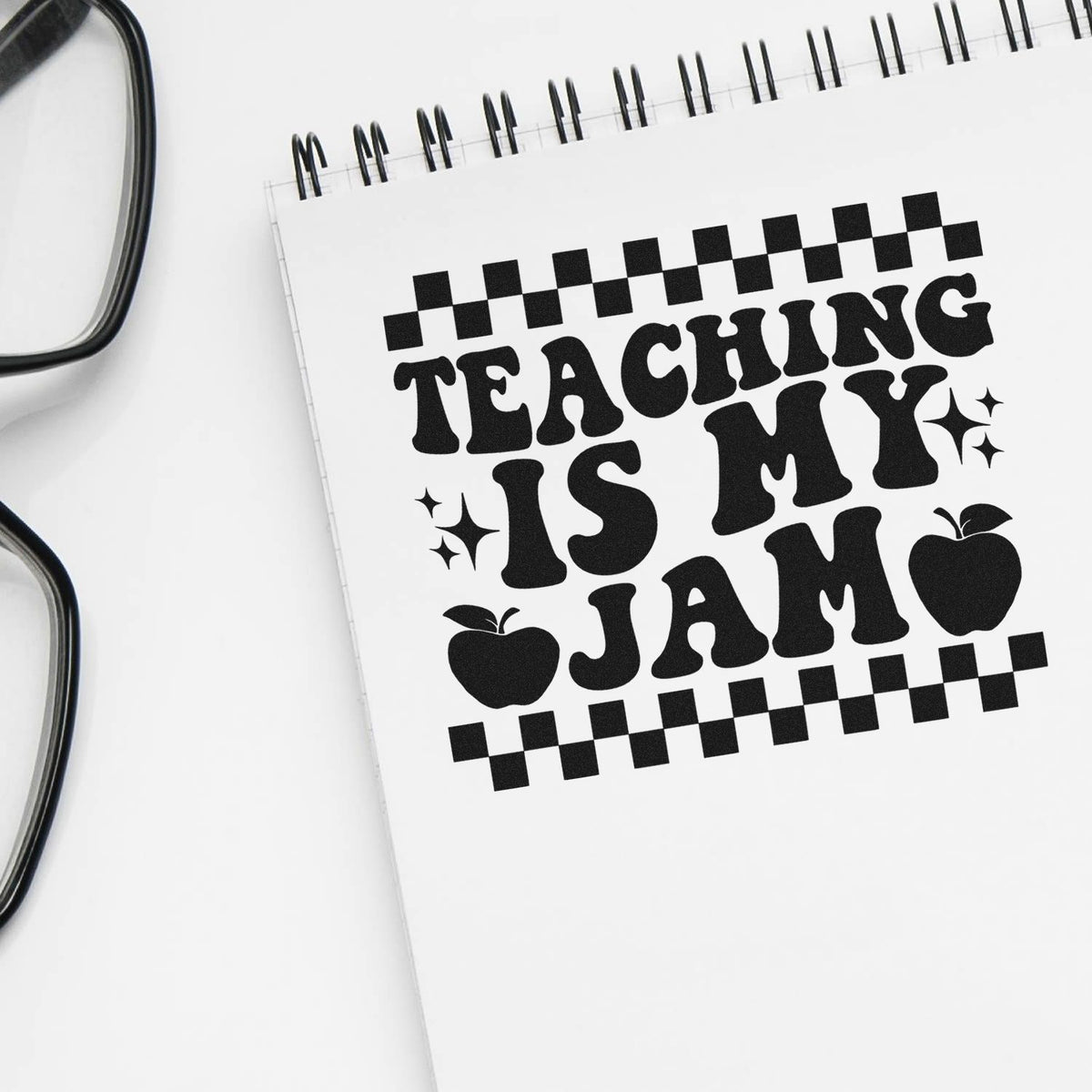 Black teaching stamp/seal design on a white spiral notebook, with checkerboard border, apples, and sparkles.