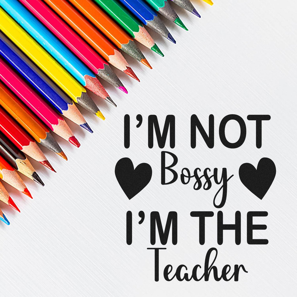 Colorful pencils beside a black teacher stamp and seal reading Im Not Bossy Im The Teacher with hearts on white.