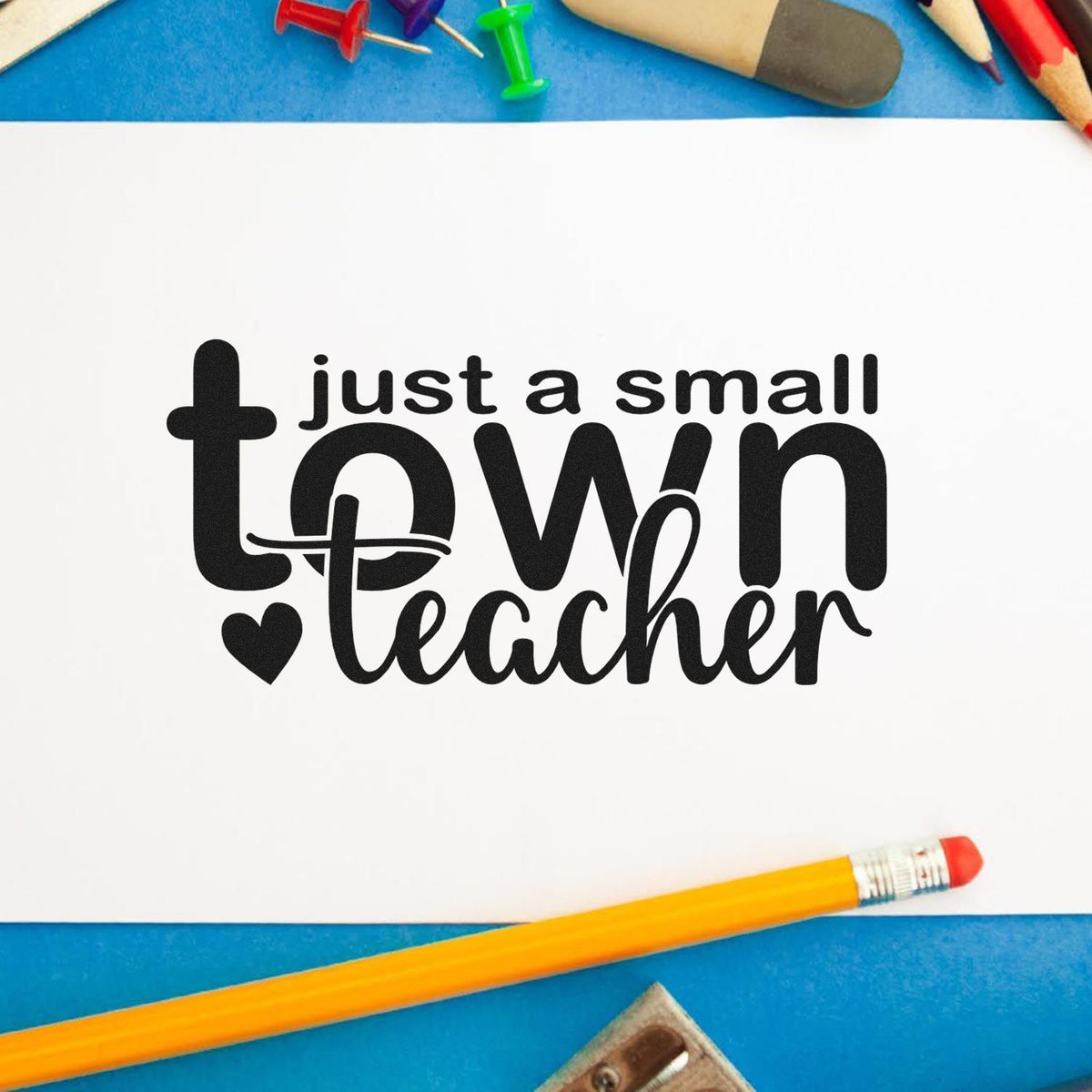 Black just a small town teacher stamp and seal design on white paper, with blue background and colorful pencils.