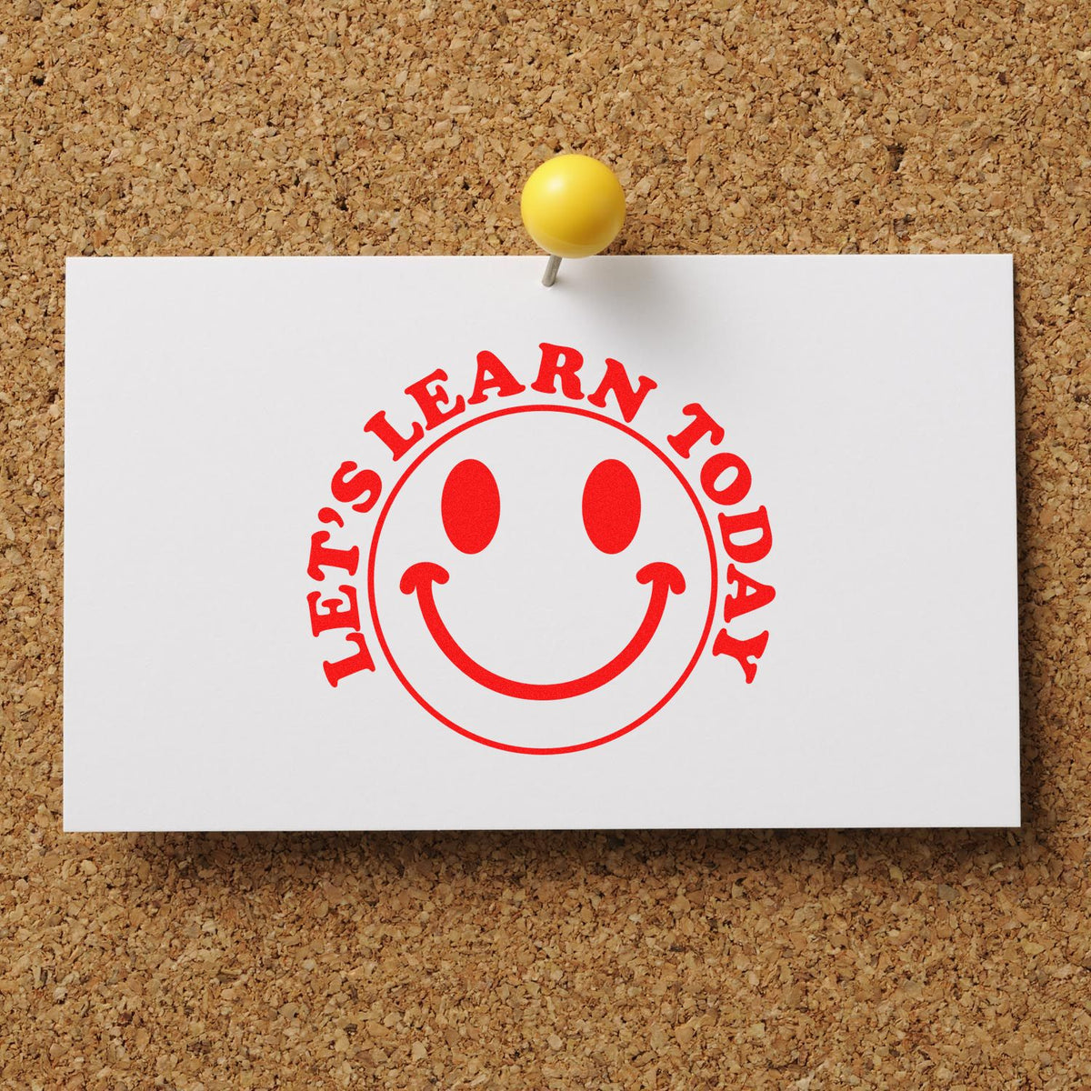 Red Lets Learn Today smiley stamp seal on white card, pinned with a yellow pushpin to a corkboard.
