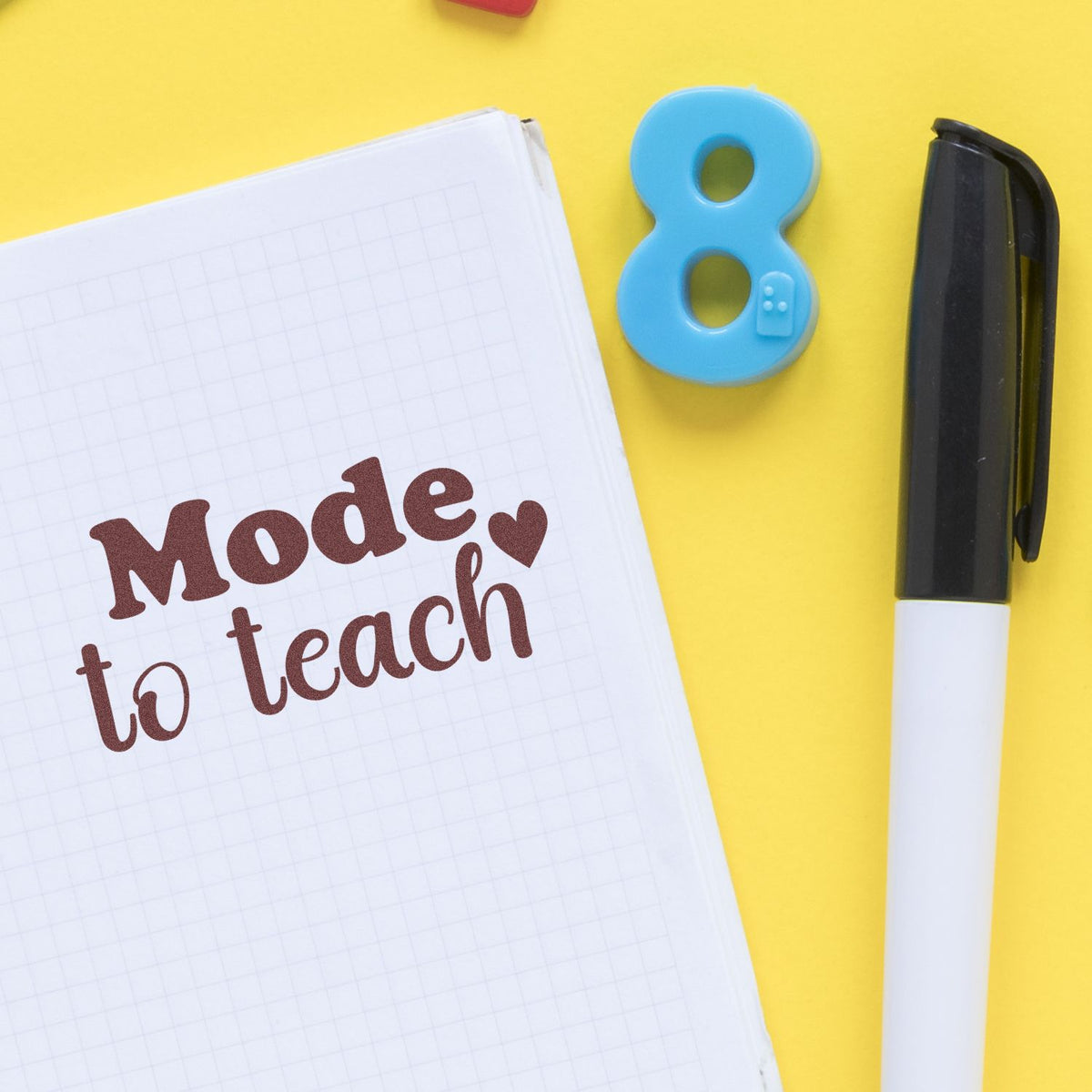 Blue number 8 stamp/seal and black marker beside a notebook reading Mode to teach on yellow background.