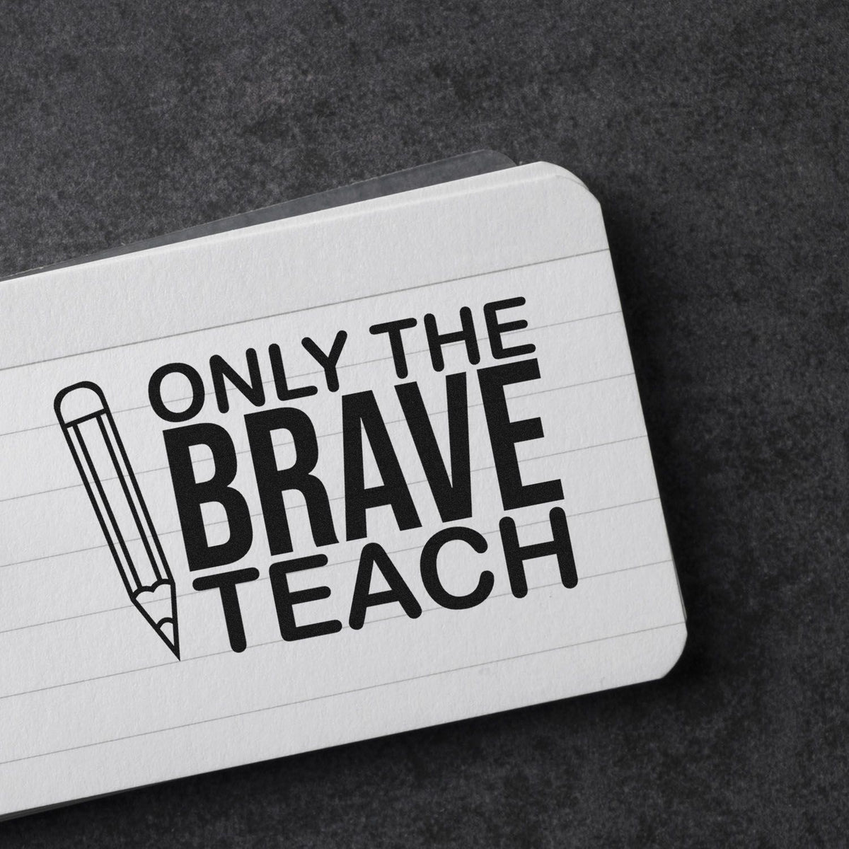 Black rubber stamp seal with pencil icon and bold text Only the Brave Teach on white lined card.