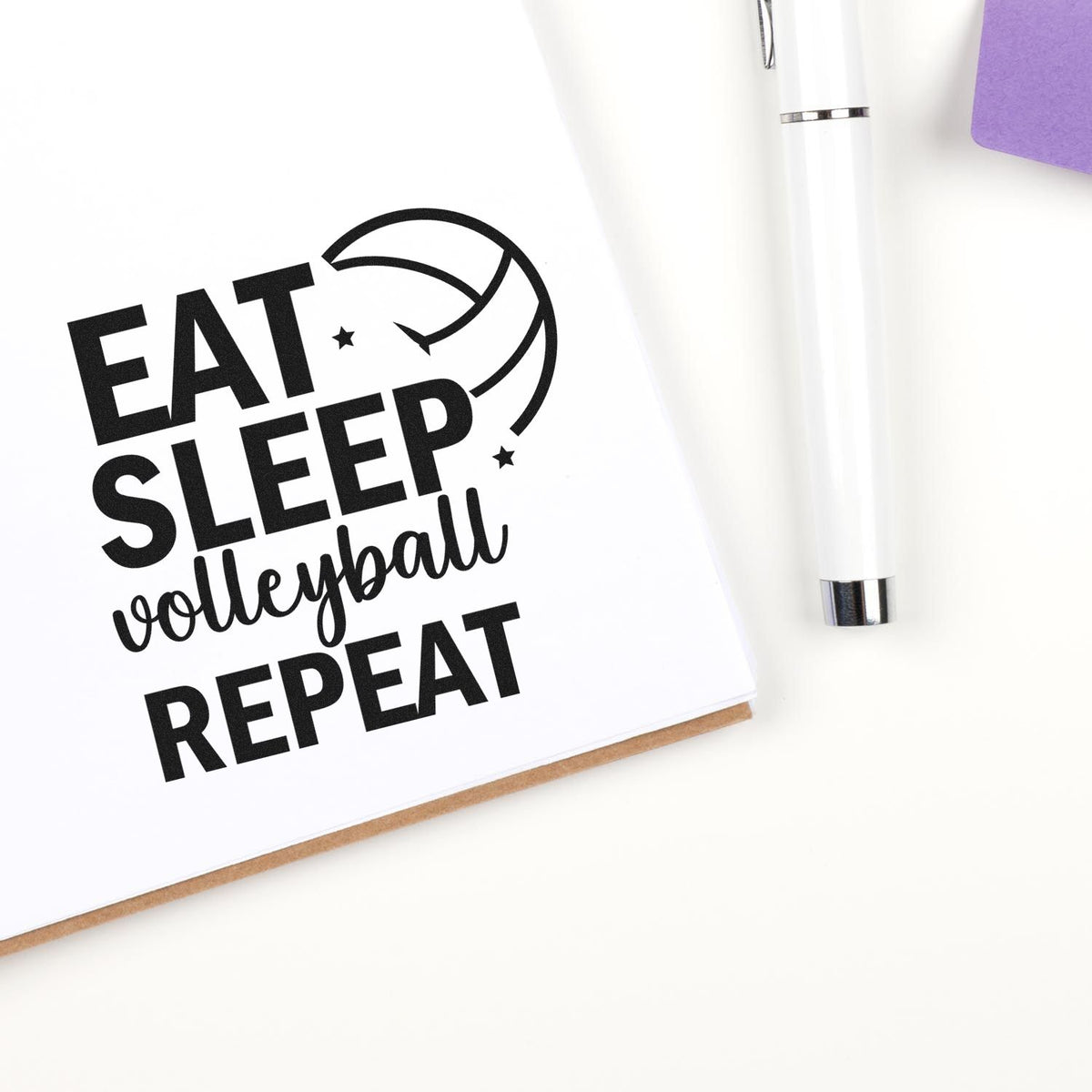 Black volleyball stamp design reading EAT SLEEP volleyball REPEAT beside a white stamp and seal pen on white paper.