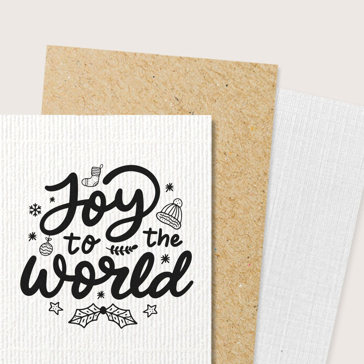 Black Joy to the World holiday stamp on white textured paper, with festive icons, beside tan kraft and white cardstock seals.