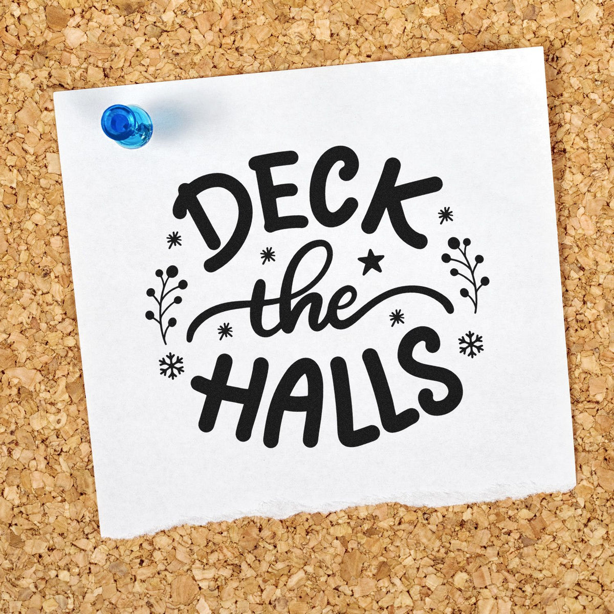 Decorative black stamp and seal reading Deck the Halls on white paper, pinned with a blue pushpin over a corkboard.