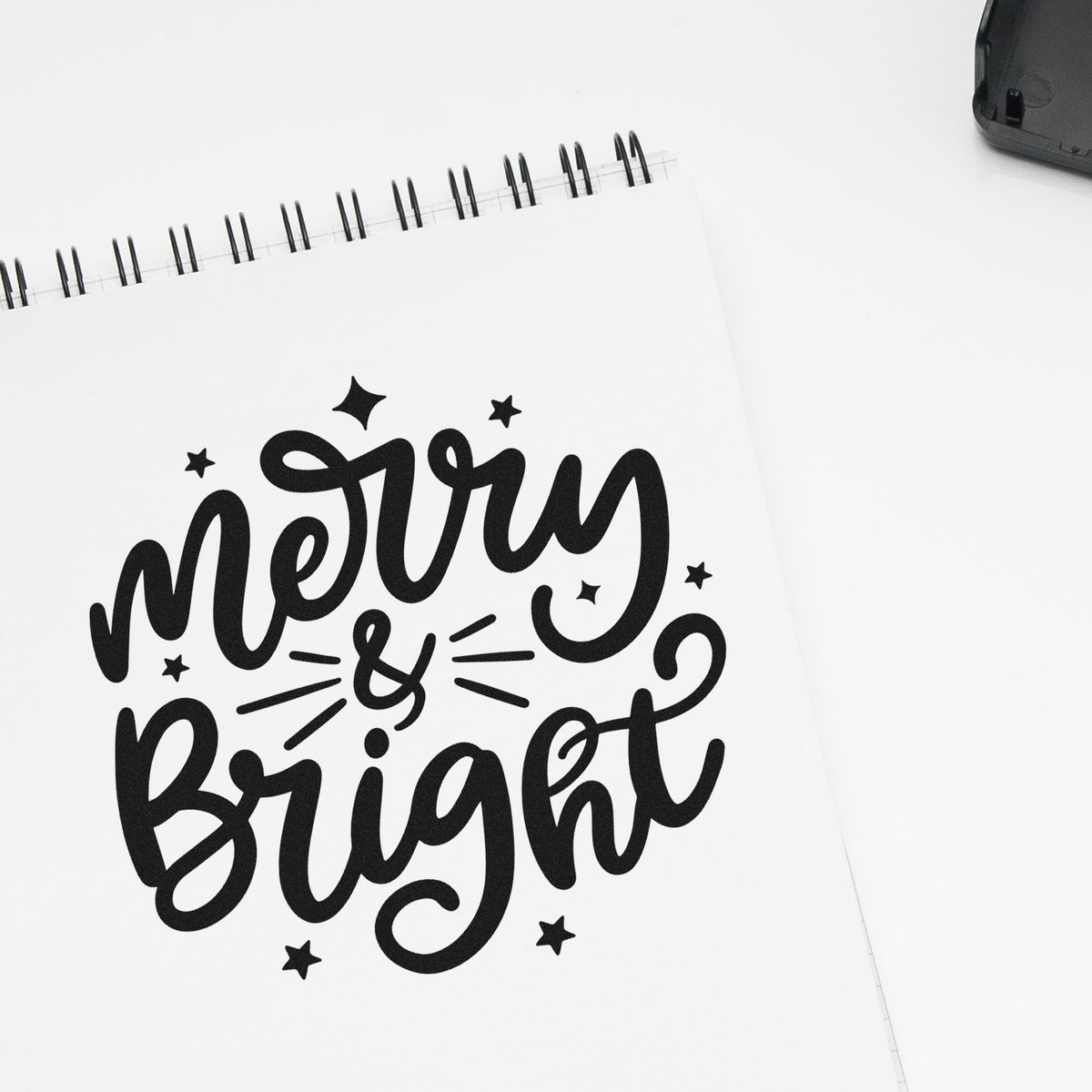 Black Merry & Bright custom stamp and seal design with stars on a white spiral notebook