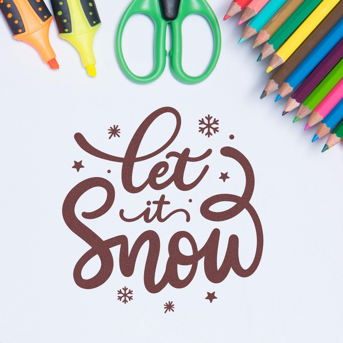 Brown Let it Snow stamp seal with snowflakes, framed by colorful pencils, highlighters, and green scissors.