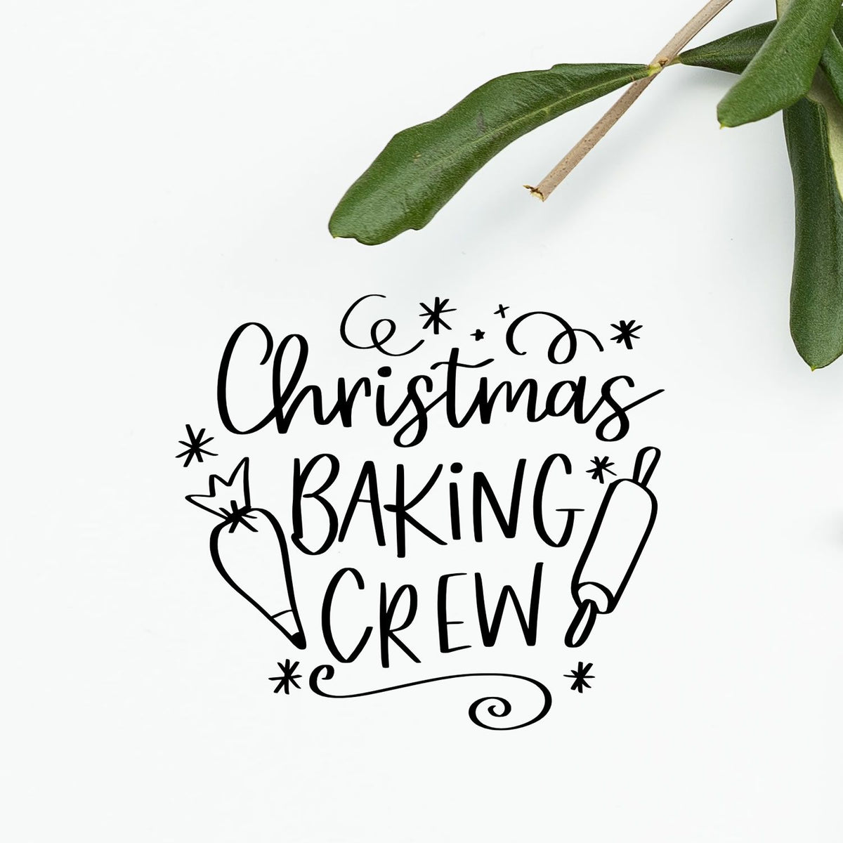 Black Christmas Baking Crew stamp design with rolling pin and whisk, on a white background with green leaves.