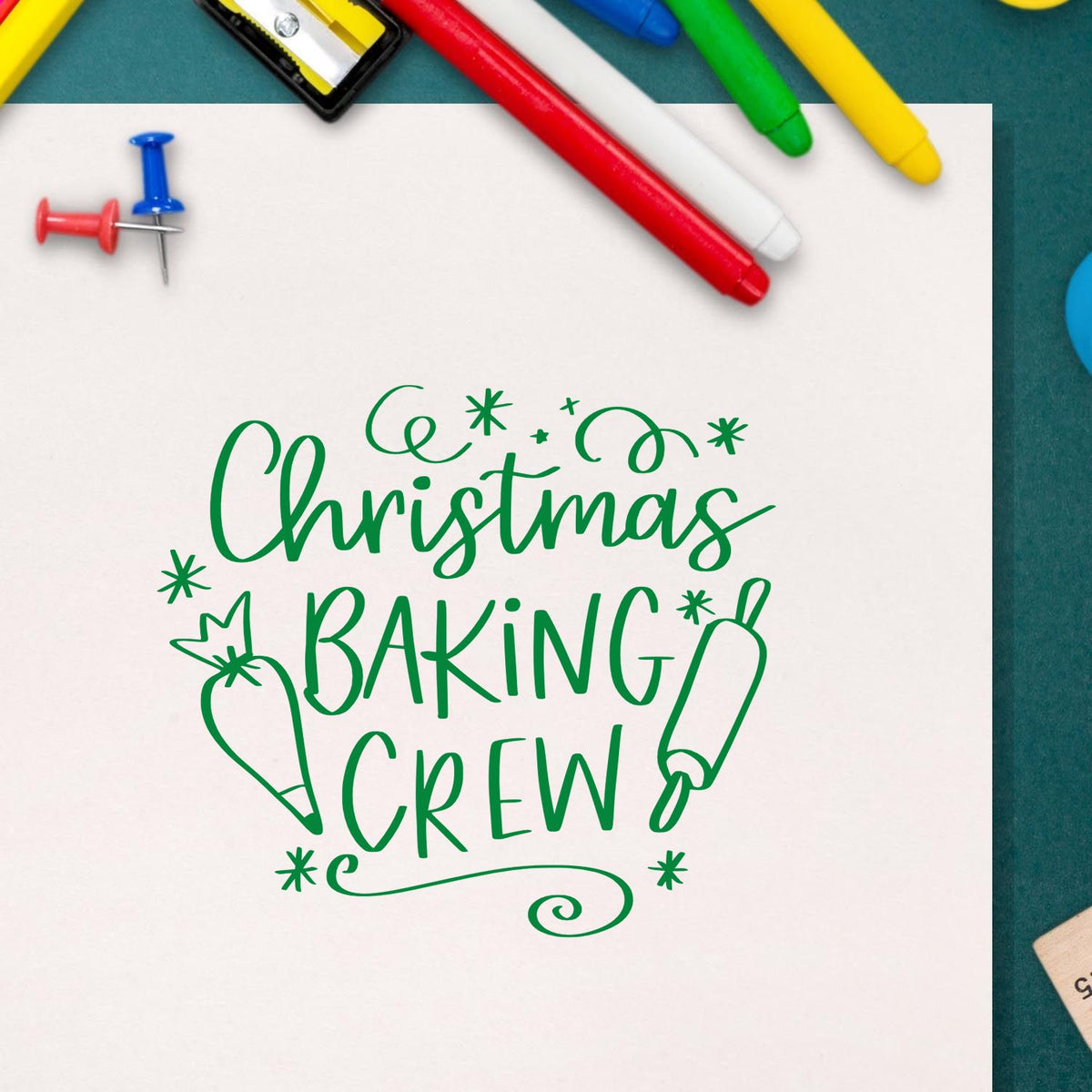 Green Christmas Baking Crew stamp and seal design on white paper, with rolling pin and whisk icons, surrounded by colorful markers.