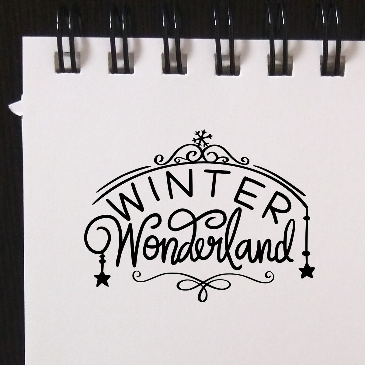 Black decorative Winter Wonderland stamp seal on white paper, with snowflake, stars, and swirls.