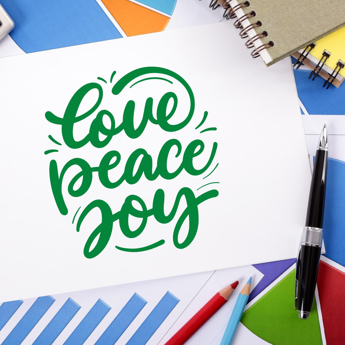 Green love peace joy stamp/seal design on white card, surrounded by blue, yellow, red, and green stationery.