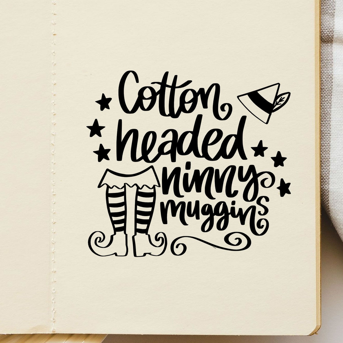 Black cotton-headed ninny muggins stamp and seal design with elf legs, hat, and stars on cream background.
