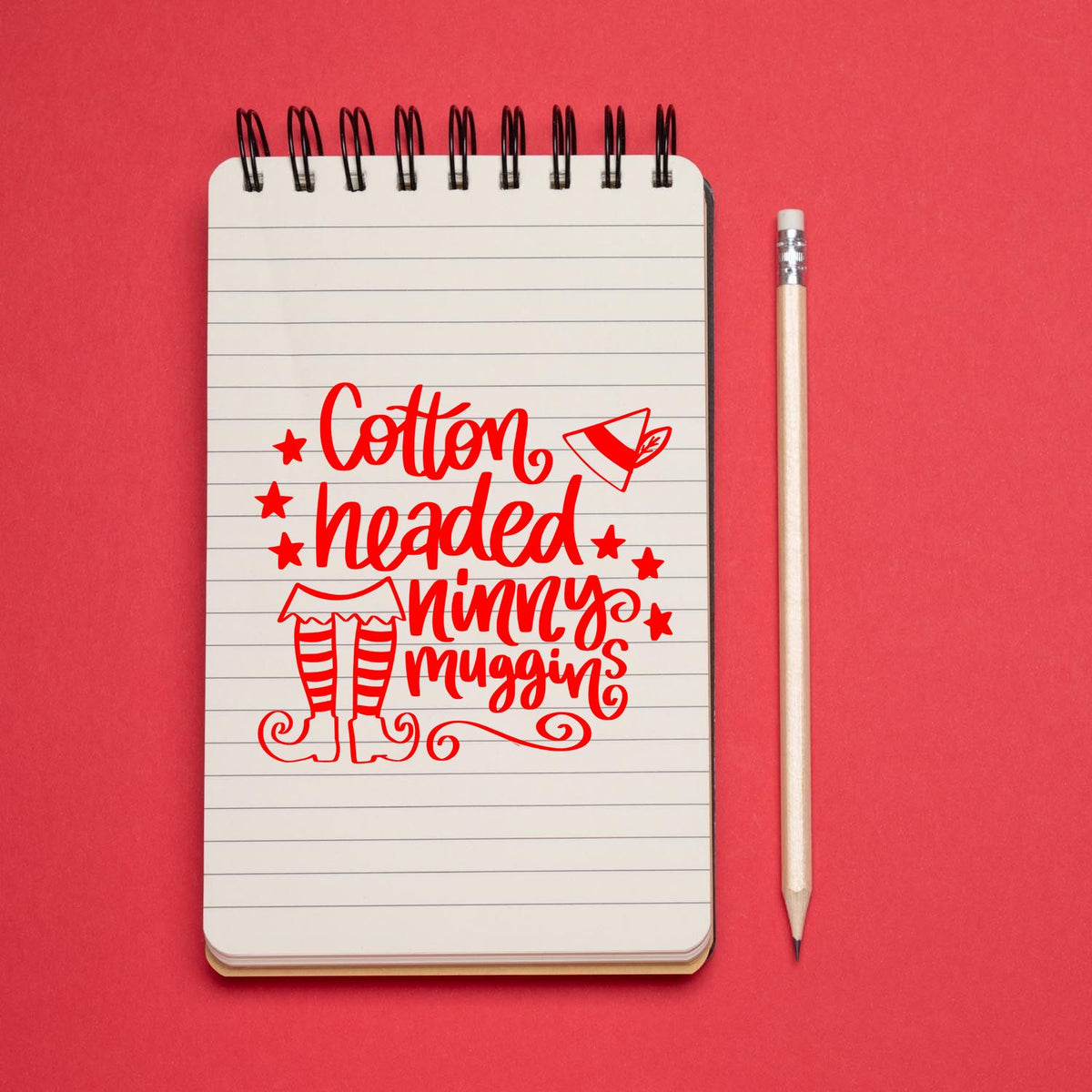 Custom stamp and seal design: red Cotton-headed Ninny Muggins text with elf legs on a lined spiral notebook, beside a pencil.