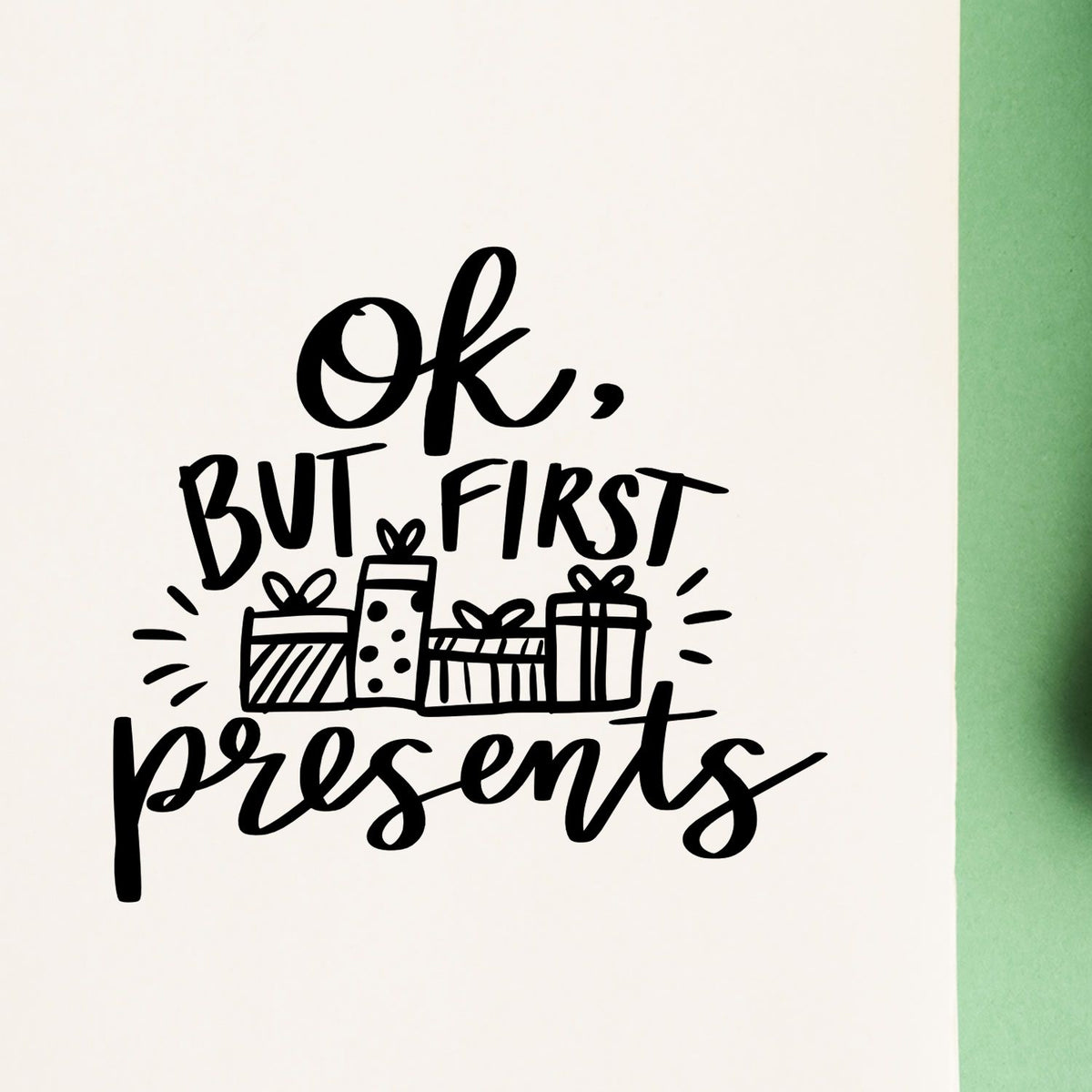 Black holiday stamp/seal reading Ok, but first presents with gift boxes on white paper and green border.