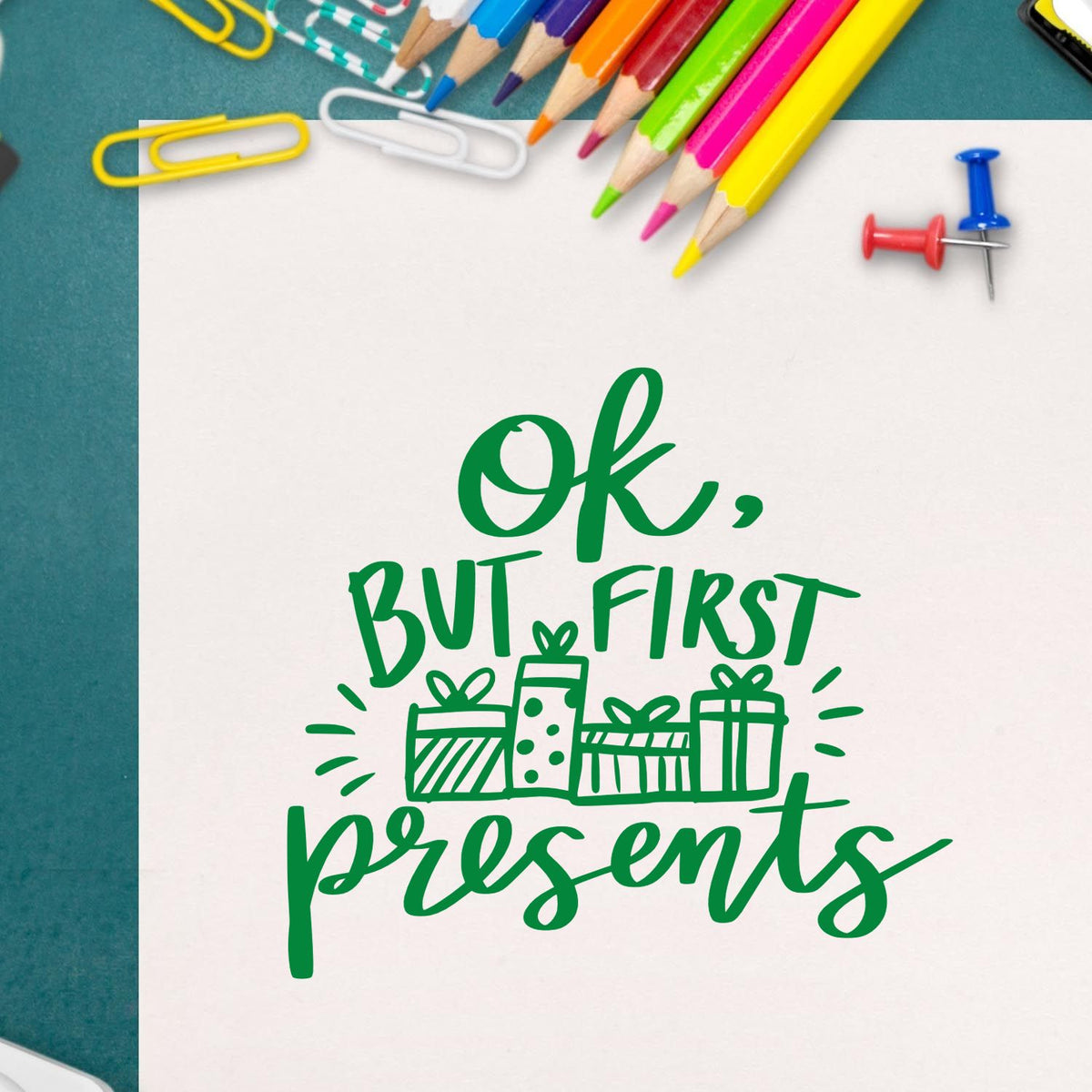 Green gift stamp and seal design reading Ok, but first presents on white paper, with colorful pencils and paper clips.