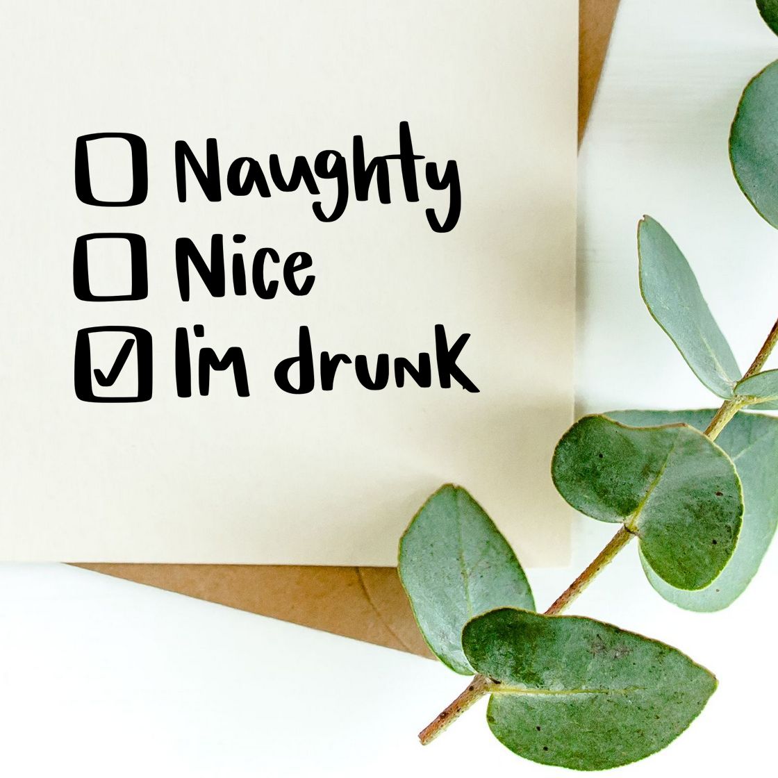 Black rubber stamp design with checkbox text Naughty, Nice, Im drunk on cream paper, accented by green eucalyptus leaves.