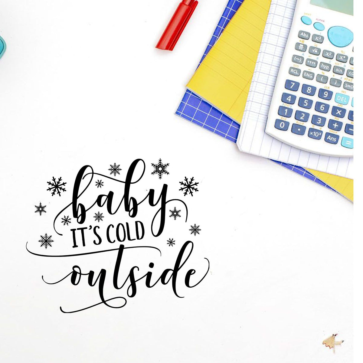 Winter stamp and seal reading baby its cold outside in black script with snowflakes, on white background with calculator and notebooks.