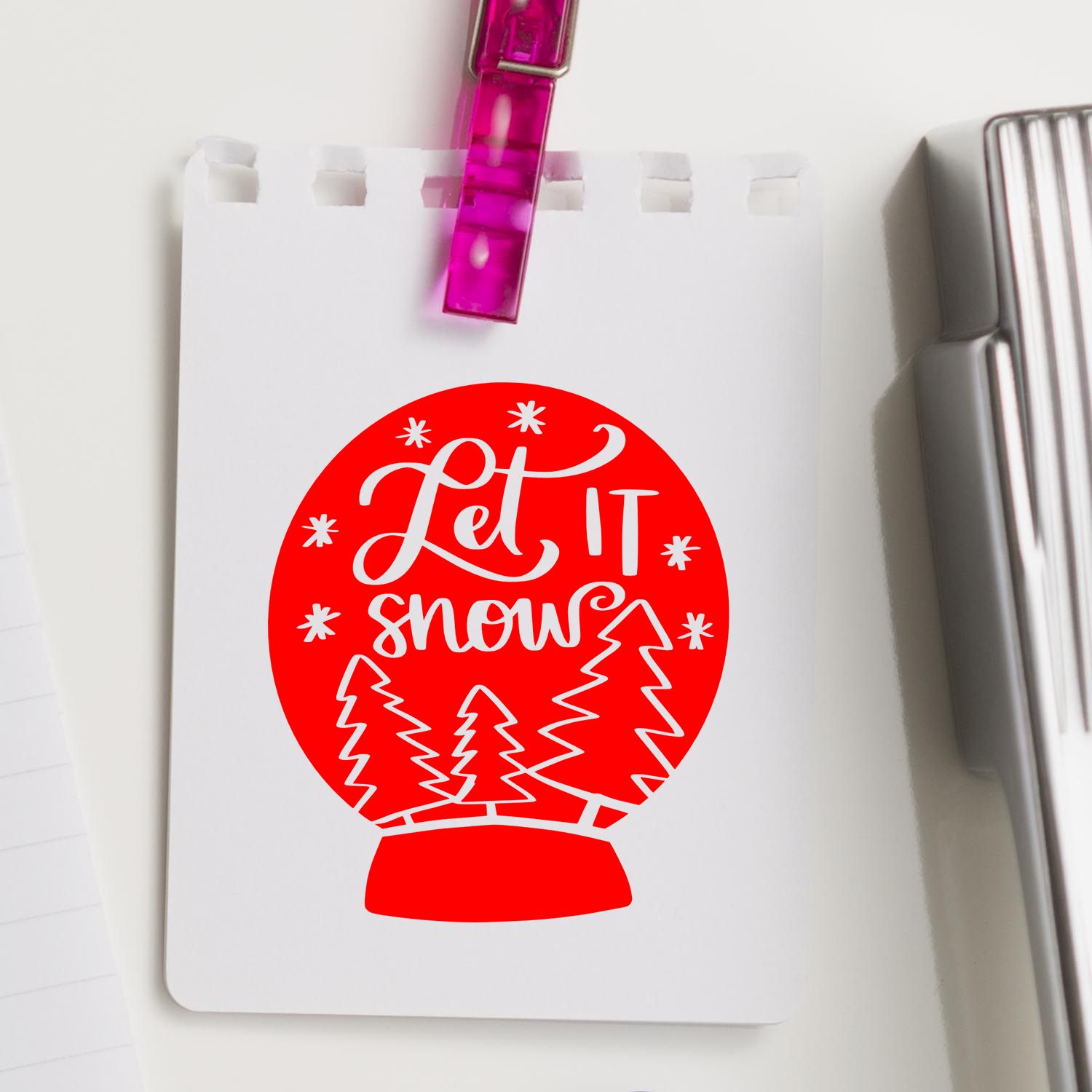 Red Let It Snow snow globe stamp design for stamp and seal products, on white card with purple clip.