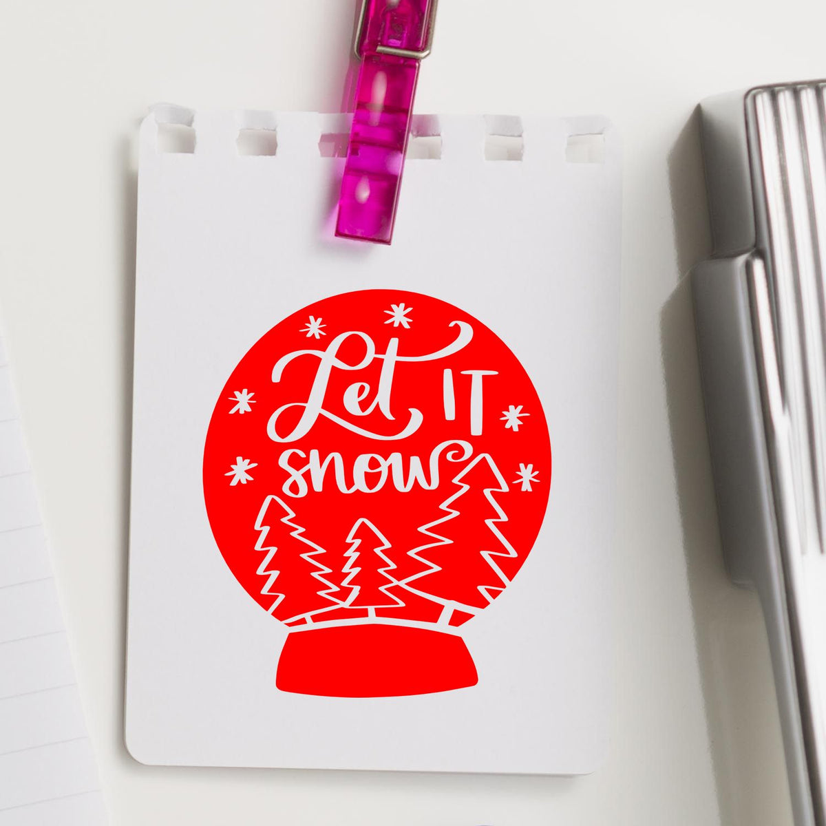 Red Let It Snow snow globe stamp on white card, clipped with pink clip, beside silver seal press