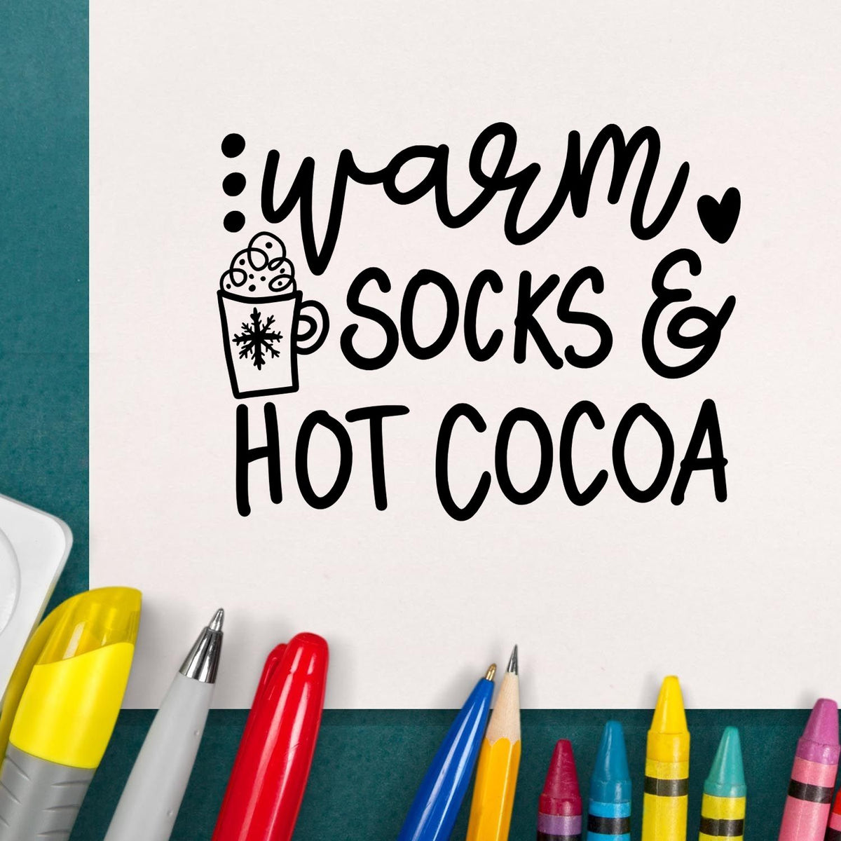 Black stamp and seal design reading warm socks & hot cocoa with mug icon, surrounded by colorful pens on teal background.