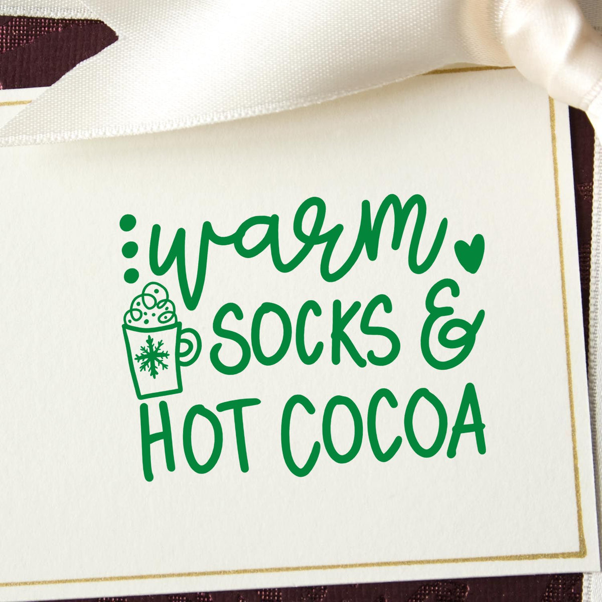 Green holiday stamp and seal design with warm socks & hot cocoa, mug icon, on white card.