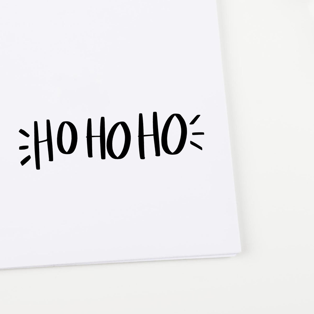 Black HO HO HO holiday stamp on white paper, with playful seal-style accents in bold black.