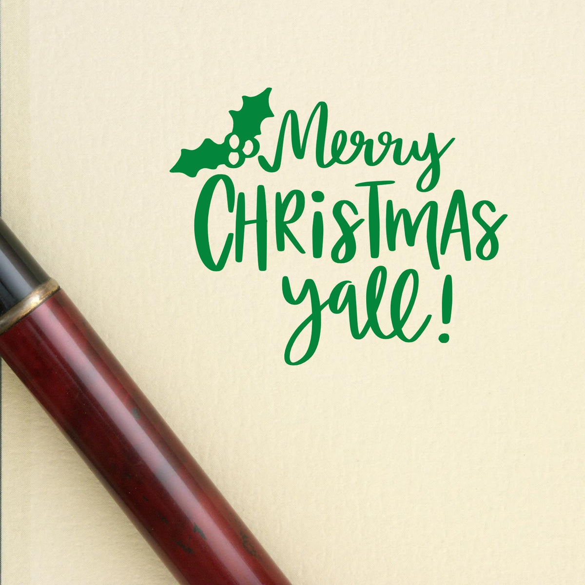 Green Merry Christmas yall holiday stamp with holly on cream paper beside a burgundy seal handle.