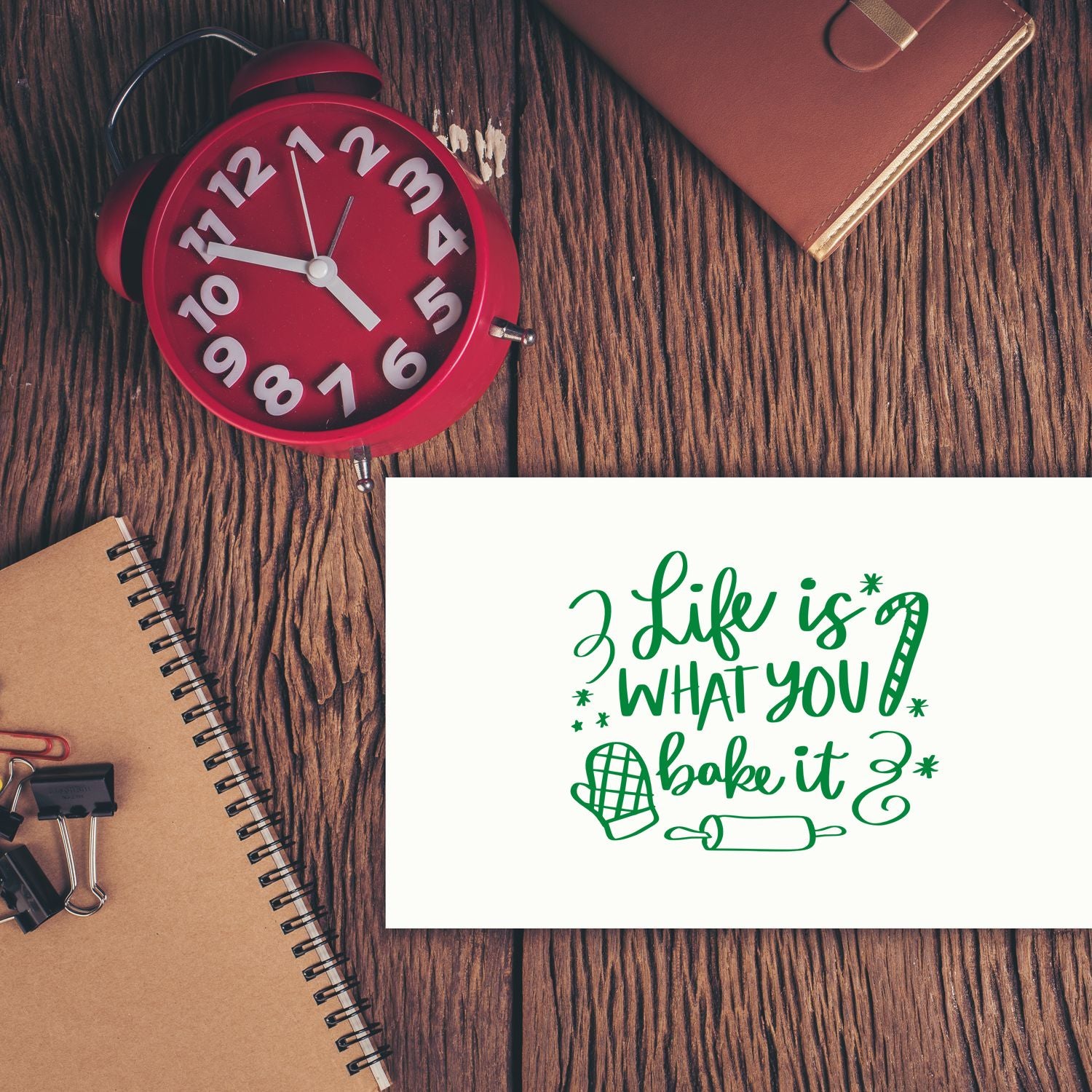 Green baking stamp and seal reading Life is what you bake it with rolling pin and oven mitt on rustic wood desk