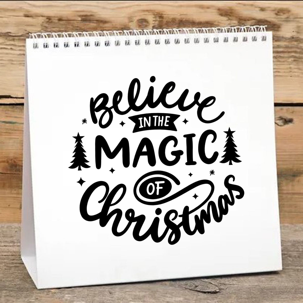 Black holiday stamp design reading Believe in the Magic of Christmas on a white bag with trees and stars.