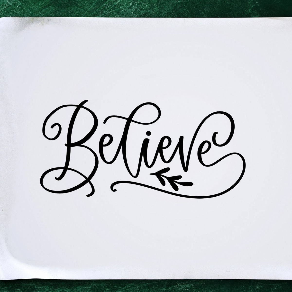 Black Believe stamp and seal design with decorative flourish on white paper, set against a green background.