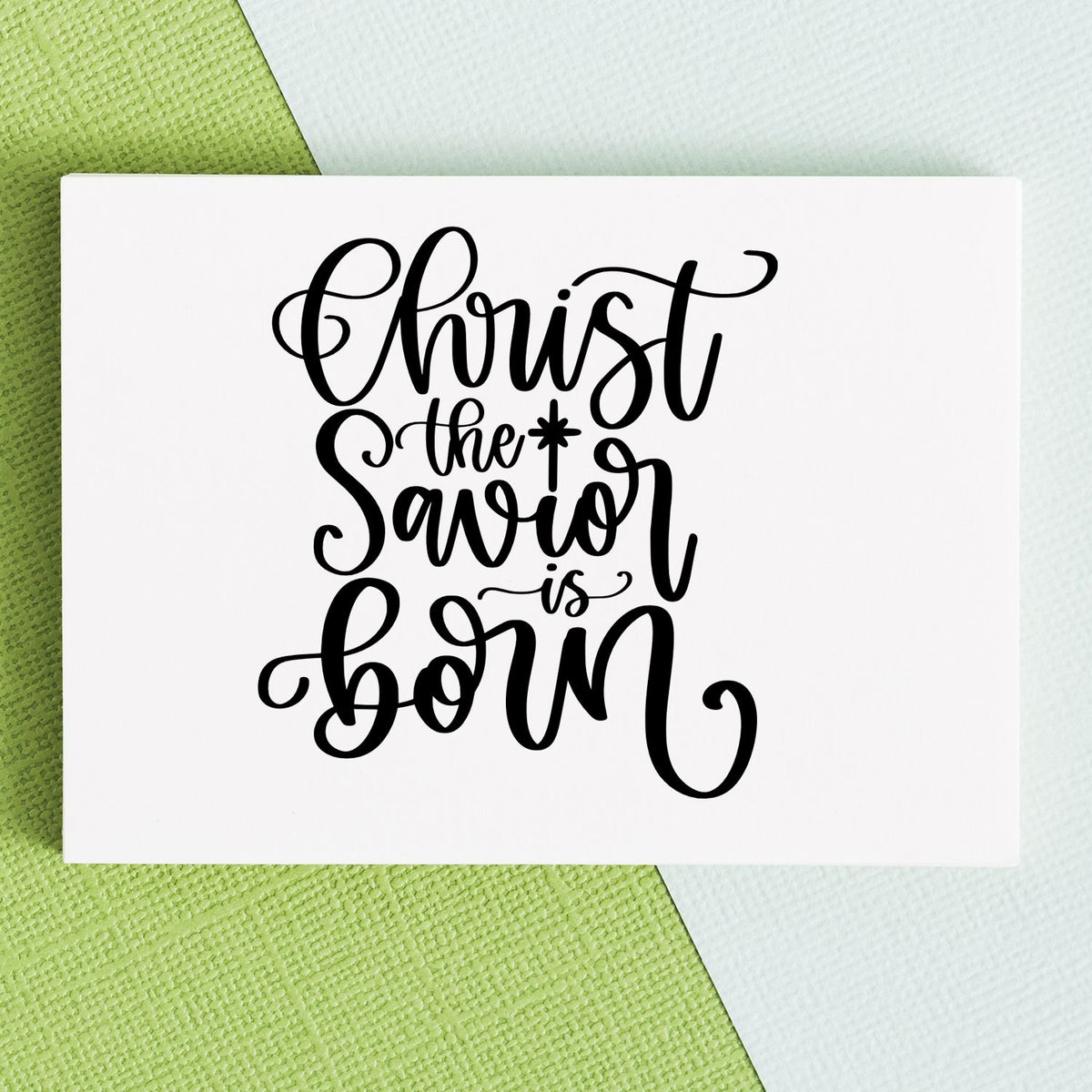 Black script Christmas stamp and seal reading Christ the Savior is born on a white card over green and white textured background.