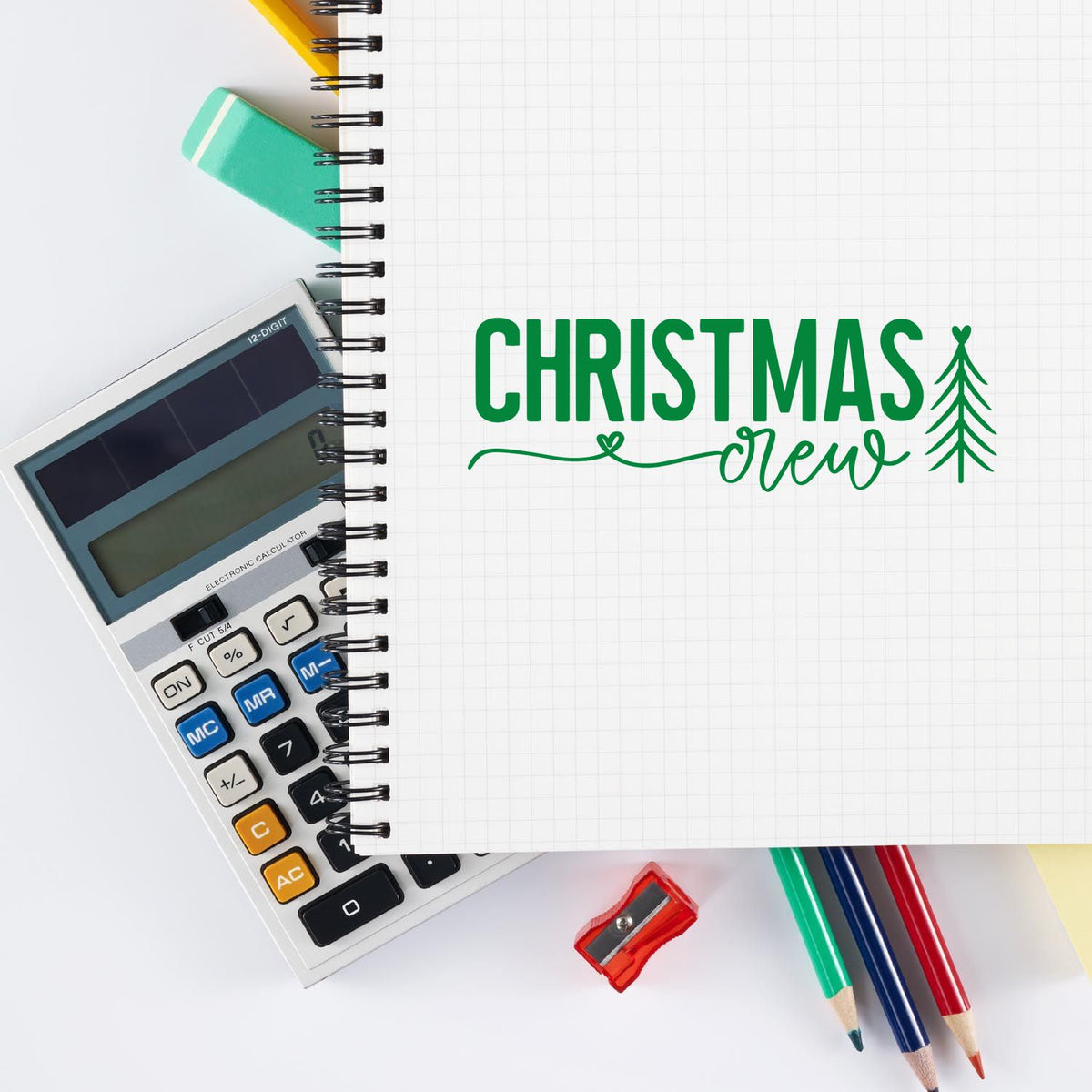 Green Christmas New stamp design on grid notebook, with calculator, pencils, sharpener and colorful office supplies.