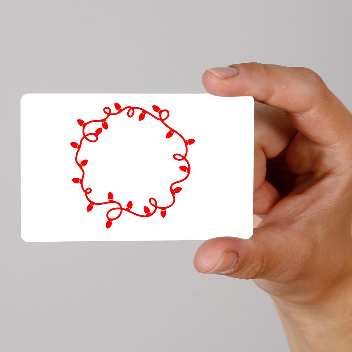Hand holding a white stamp and seal card with a red decorative light wreath border.