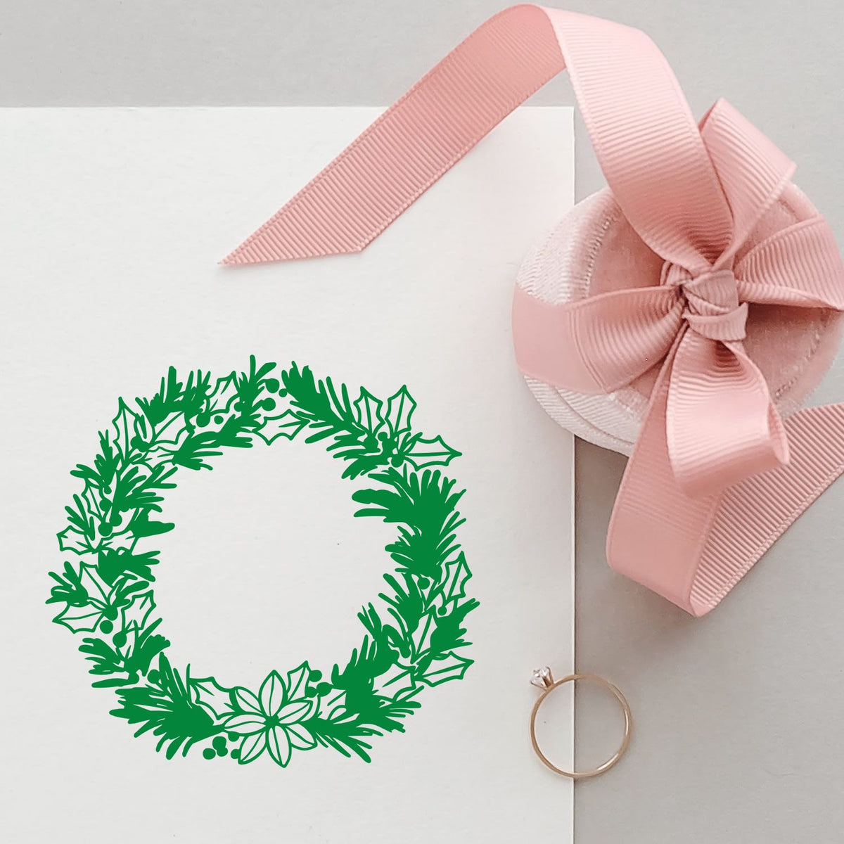 White envelope featuring a green holiday wreath stamp, pink ribbon bow seal, and gold ring accent.