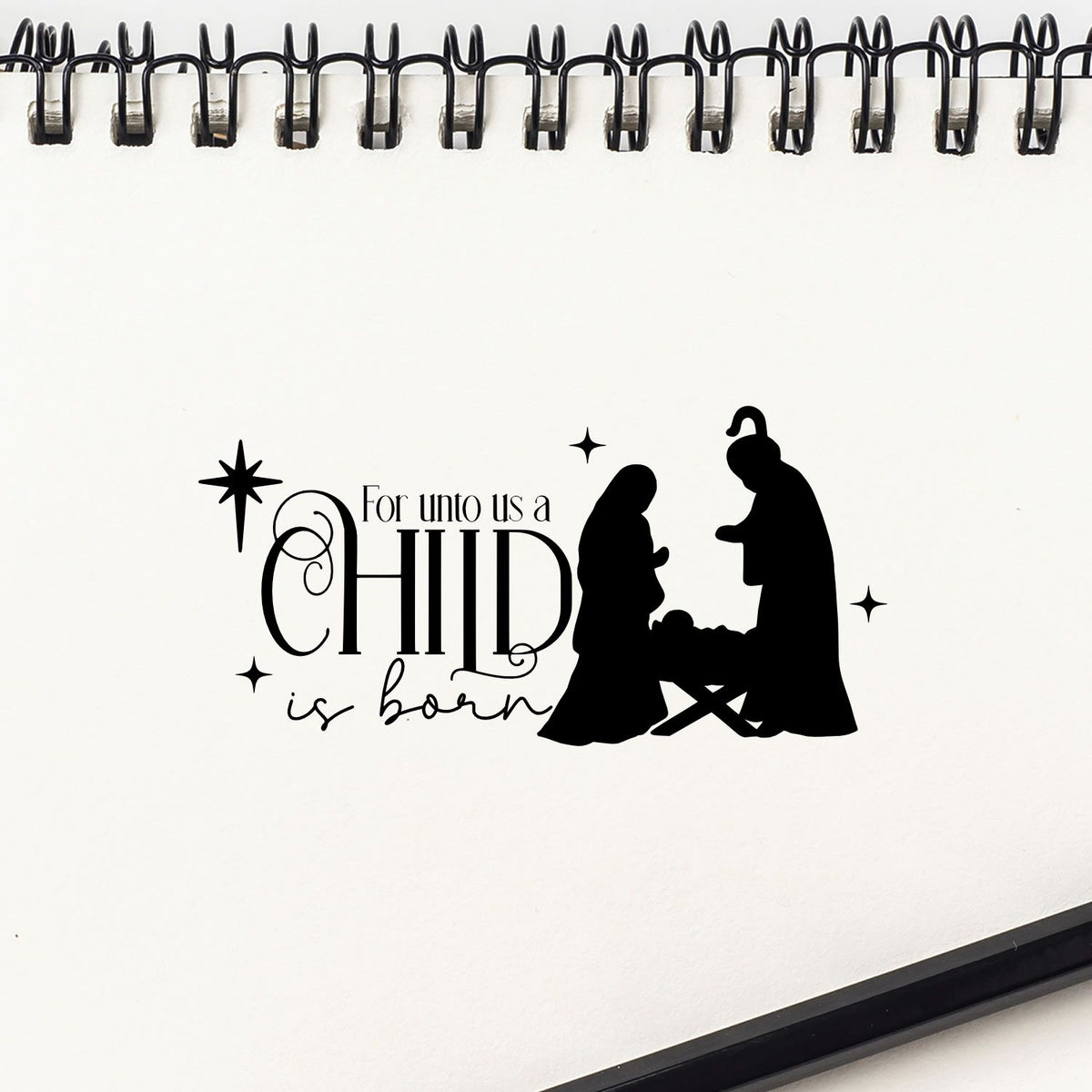 Black child is born stamp and seal design on white spiral notebook, with nativity silhouettes and decorative stars.