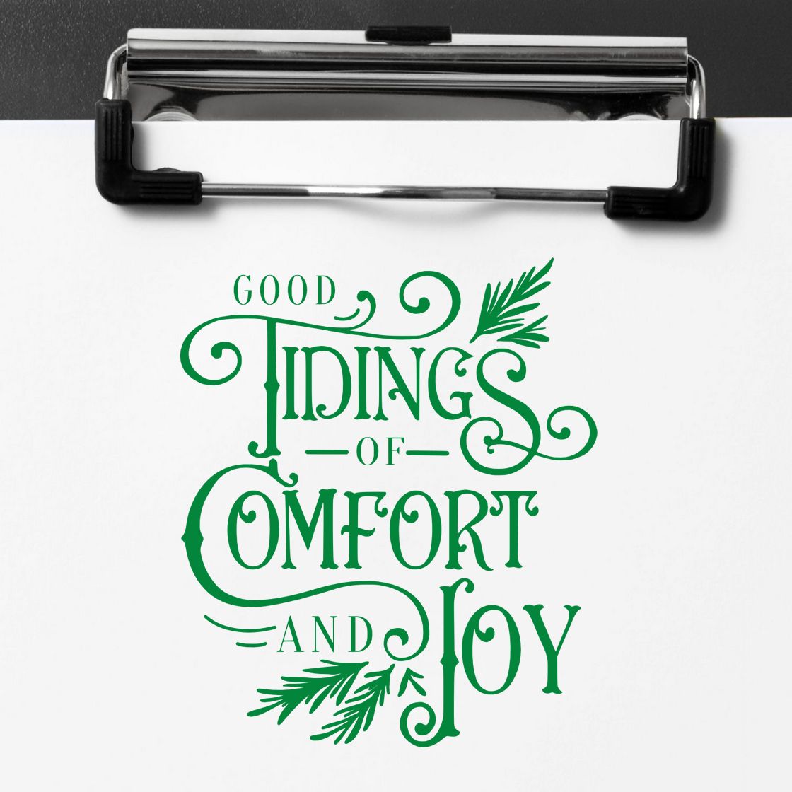 Green rubber stamp and seal on clipboard reads Good Tidings of Comfort and Joy with festive pine sprigs.