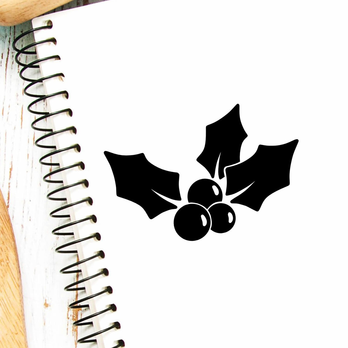 Black holly berry stamp and seal design on a white spiral notebook page with rustic wood edges.