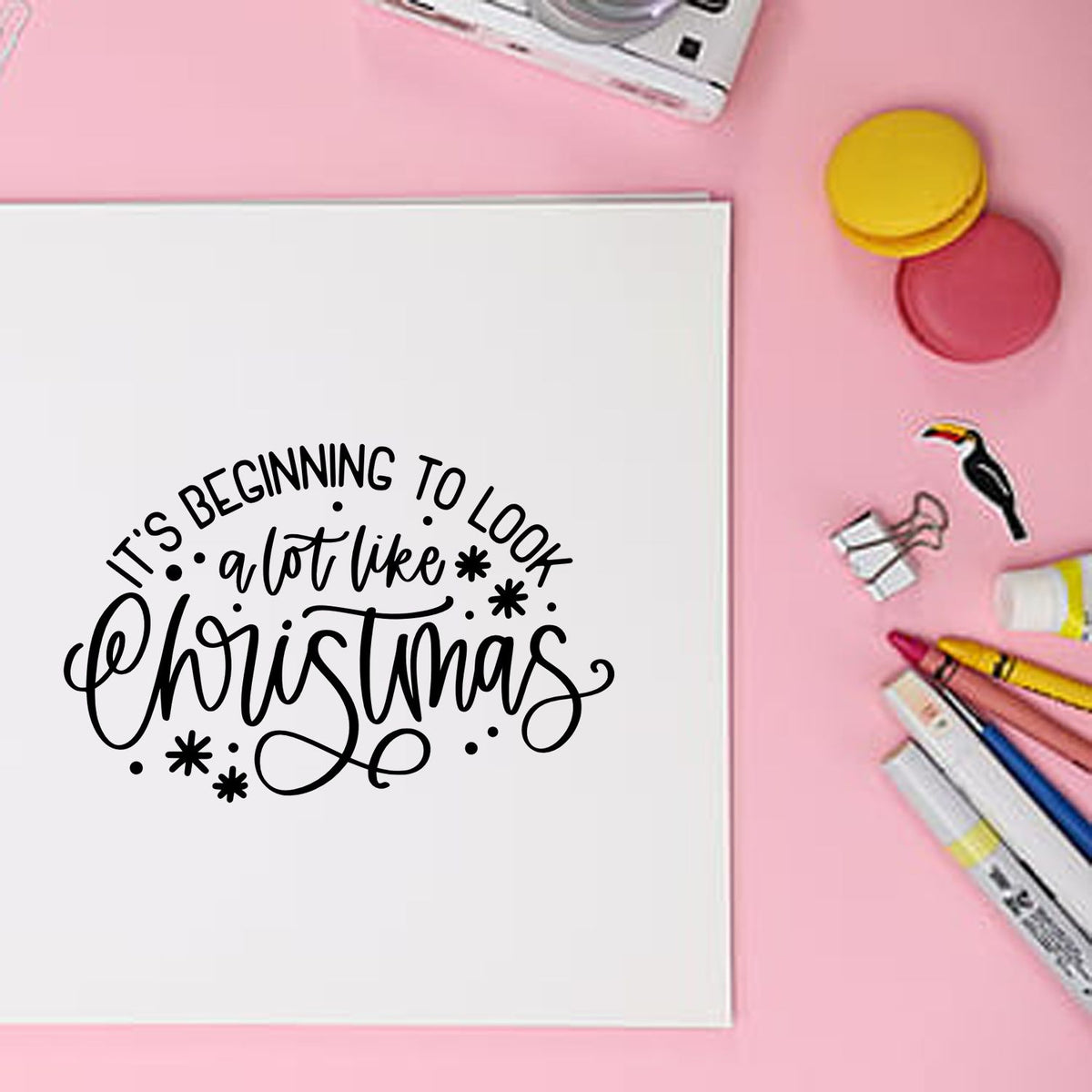 Black Christmas sentiment stamp on white card, with pink background, colorful seal discs, markers, and toucan stamp accents.