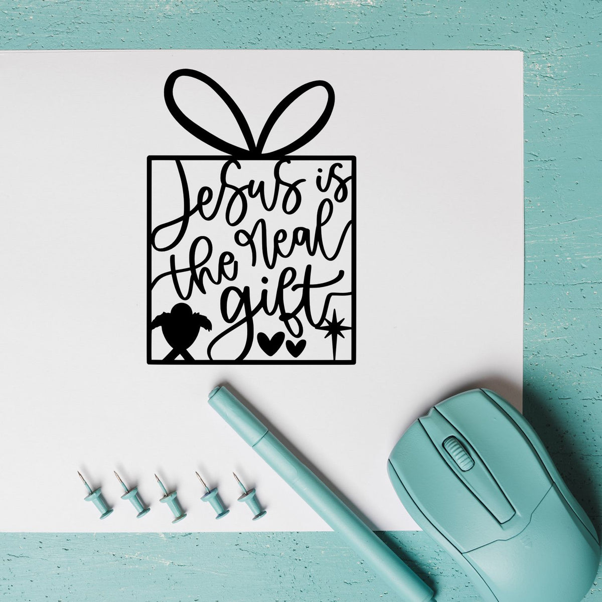 Black Jesus is the real gift gift-box stamp with bow, beside mint aqua stamp seal tools, pen, and pins on white paper.