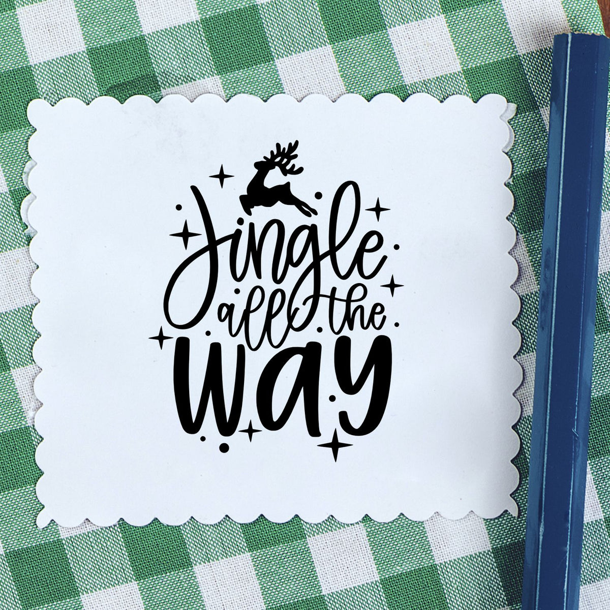 White scalloped stamp seal with black Jingle all the Way text, reindeer graphic, on green gingham background.