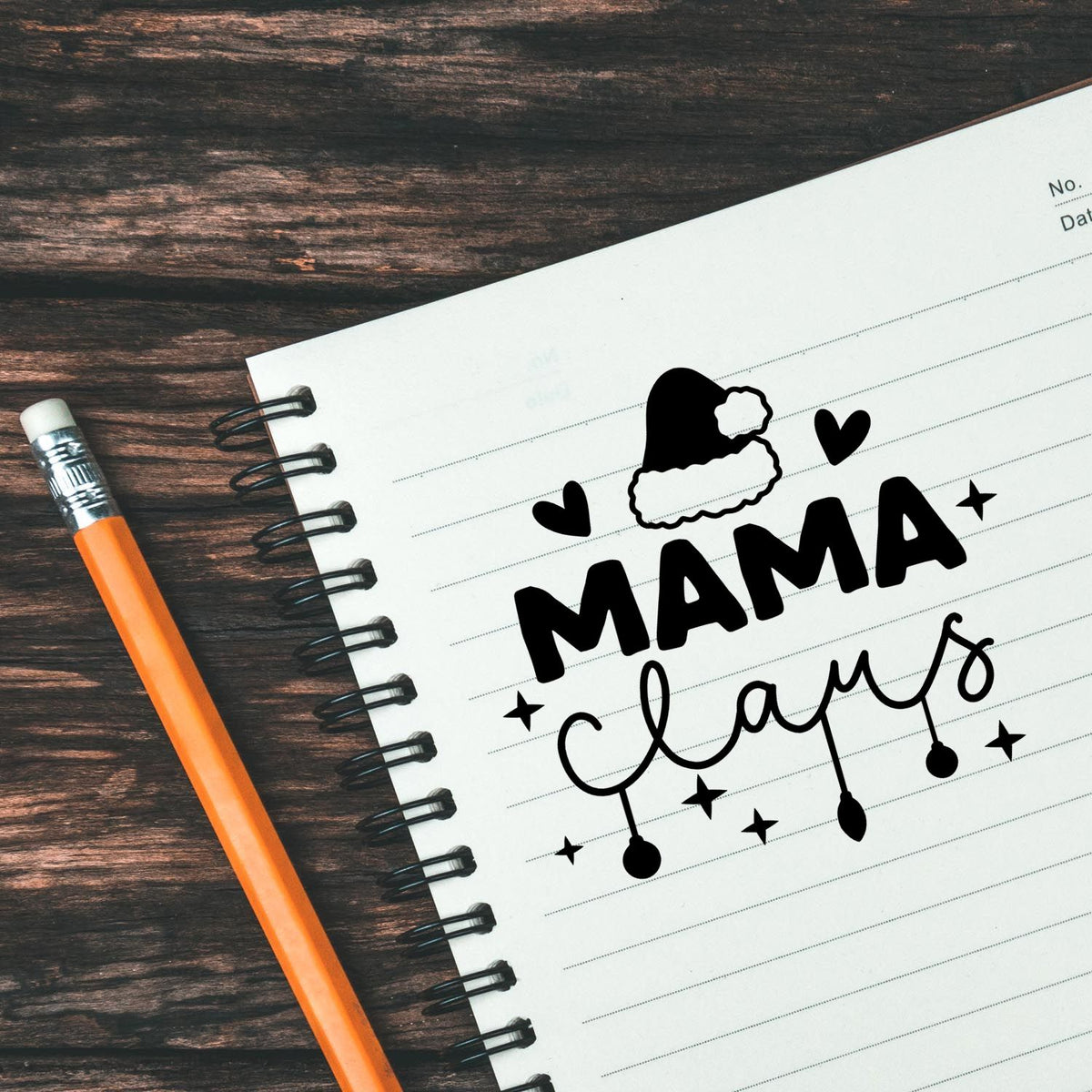 Black MAMA stamp seal with Santa hat on white notebook page, orange pencil on dark wood background