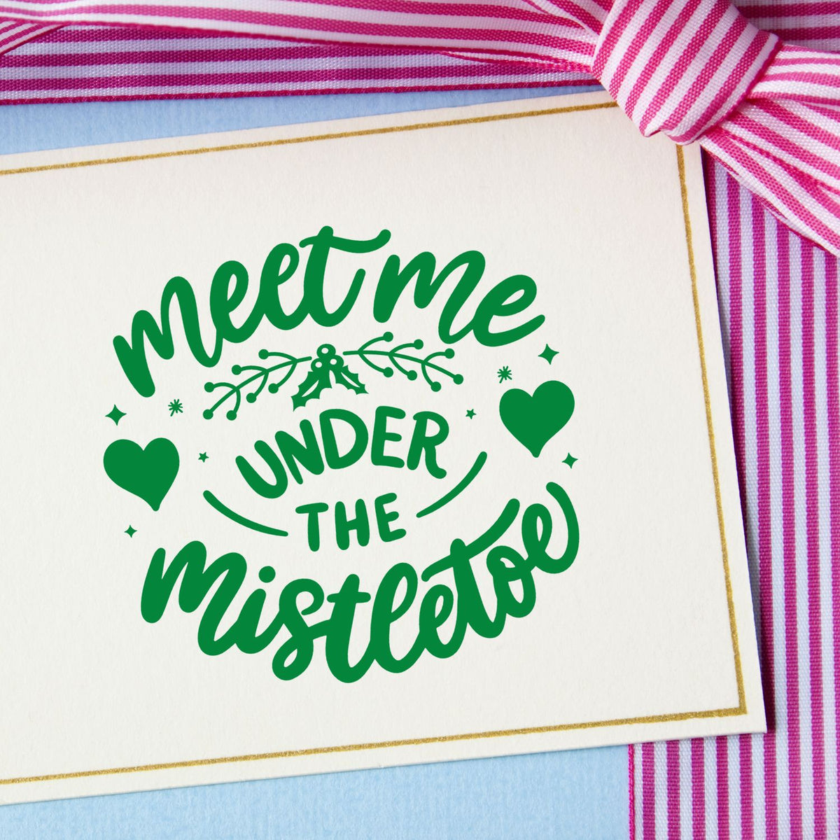 Green Meet me under the mistletoe stamp seal on white card, with gold border, hearts, and pink striped ribbon.