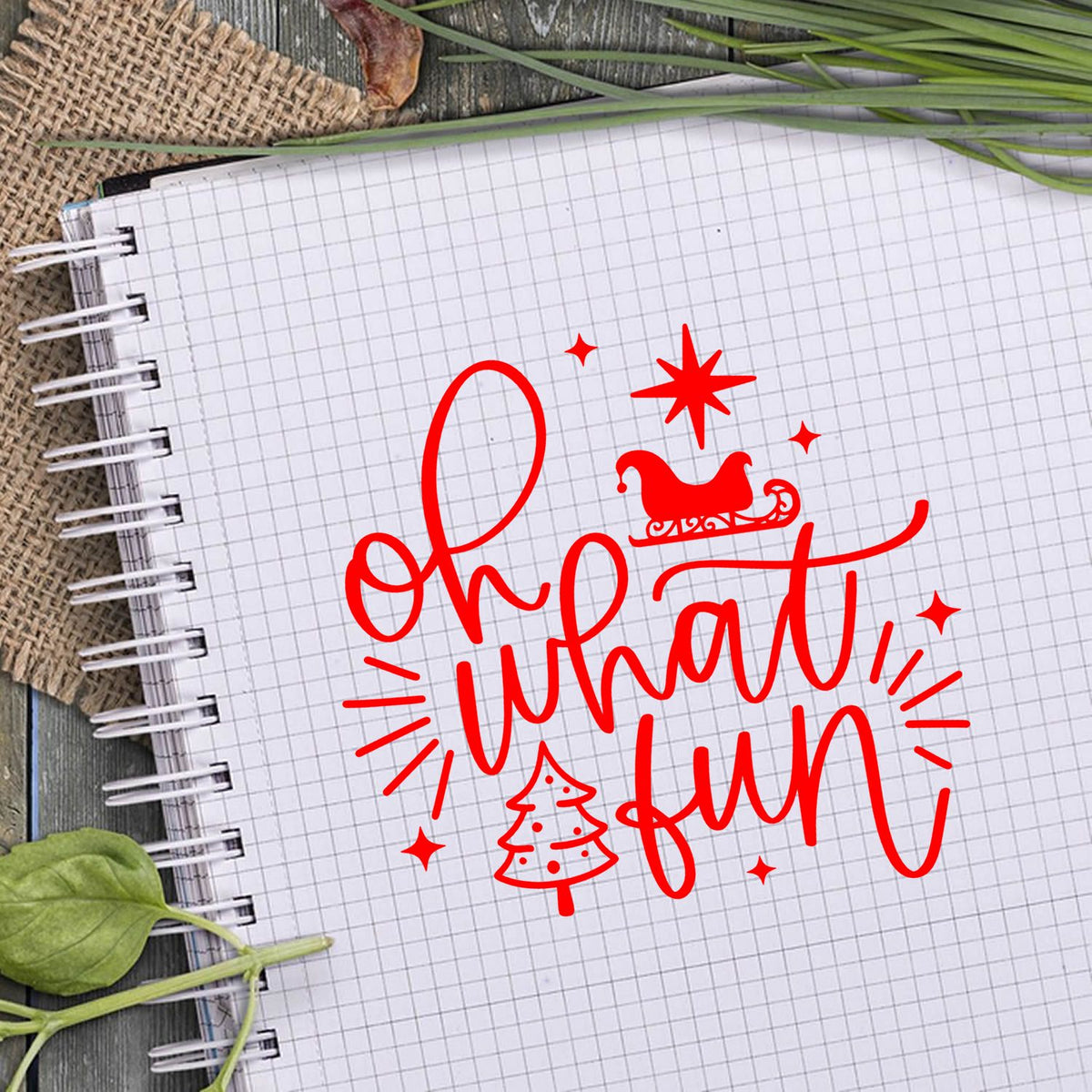 Red holiday stamp and seal reading Oh what fun with Santa hat and tree on white grid paper, with green leaves.