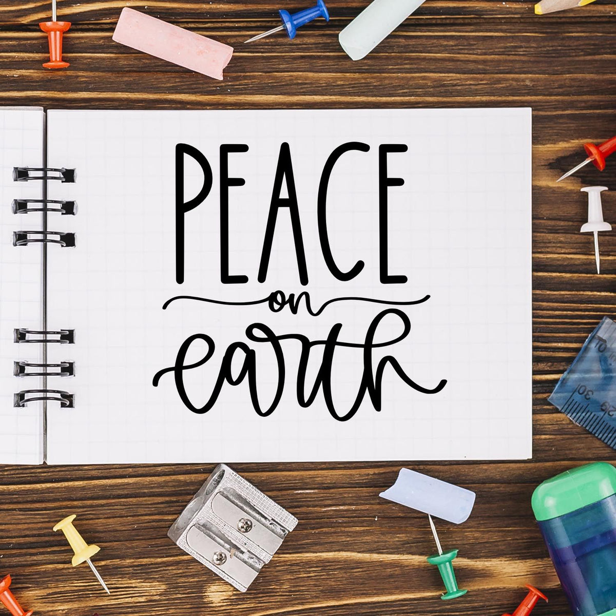 Peace on earth notebook design with colorful stamp and seal products, push pins, and school supplies on a wood desk.