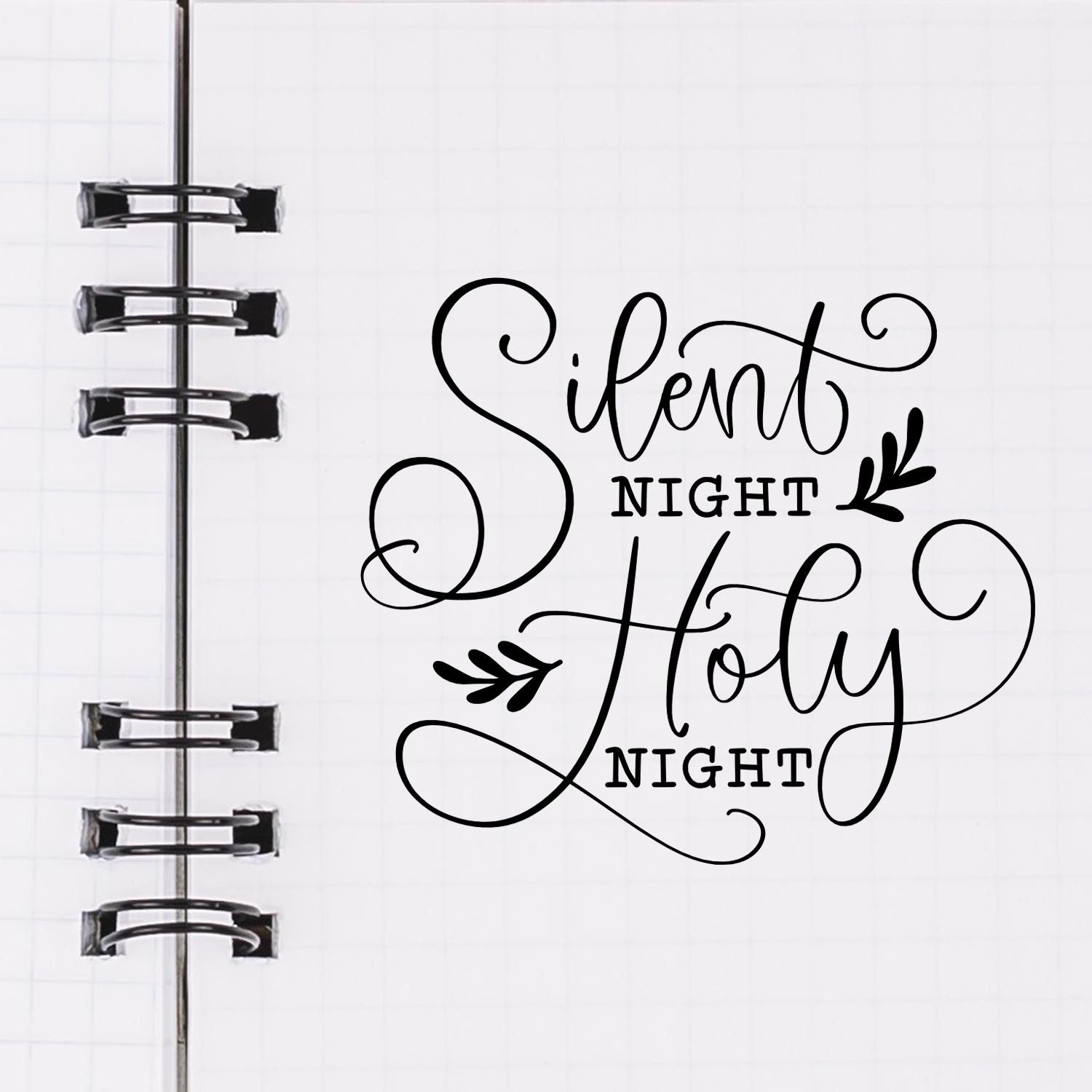 Black stamp and seal design reading Silent Holy Night on a white grid notebook page with spiral binding and leaf accents.