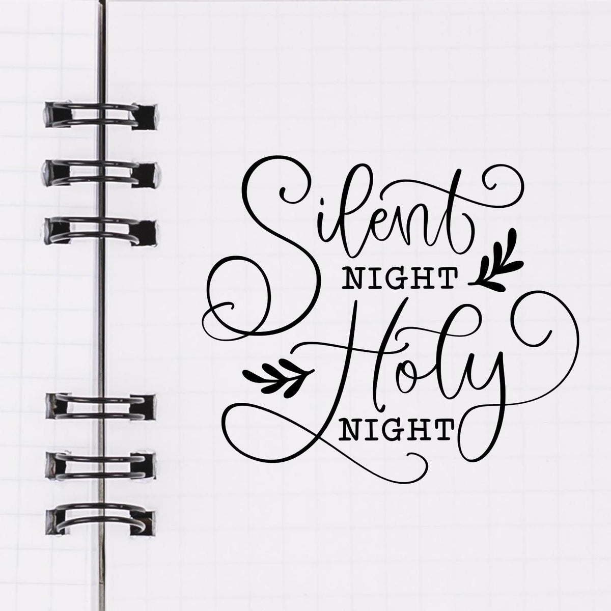 Black decorative stamp and seal reading Silent Night Holy Night on a white notebook page with spiral binding.
