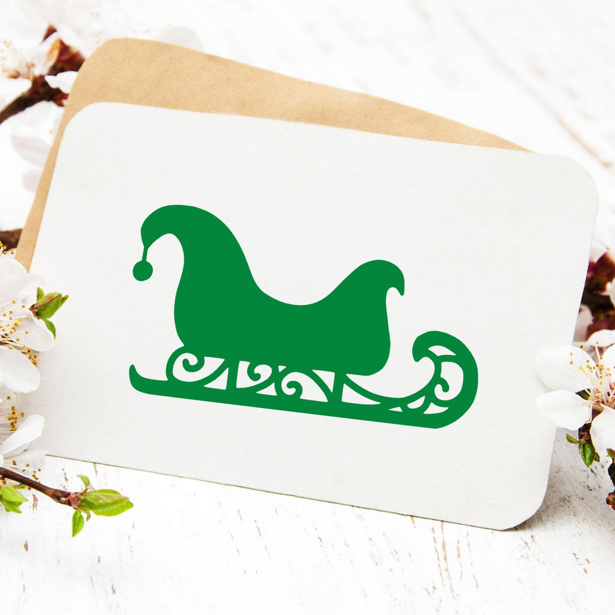 Green decorative stamp seal on a white card, with a tan envelope and white blossoms in the background.